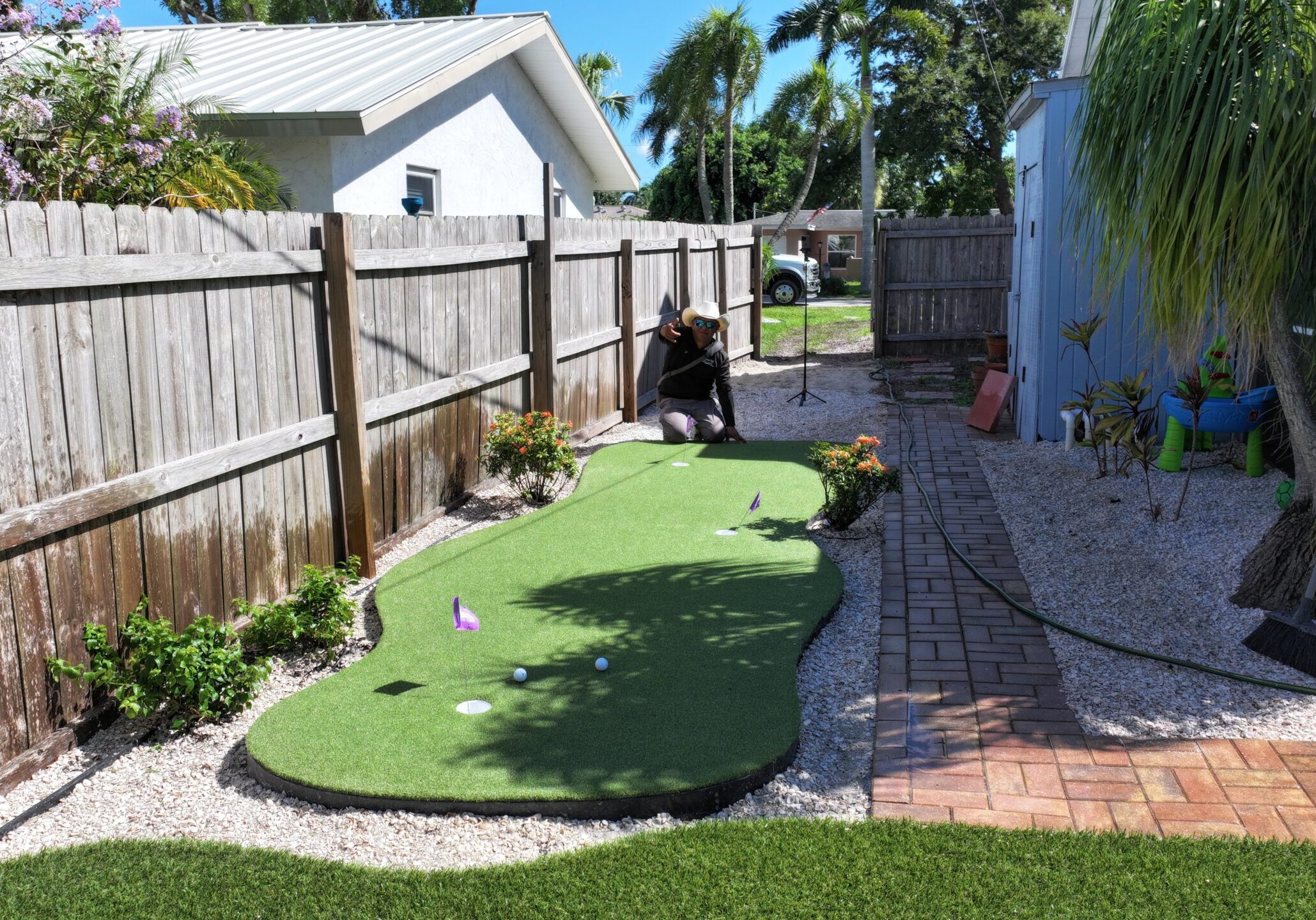 Man working for a landscaping company extending hand in front of an artificial turf golf course, showcasing the fresh installation.